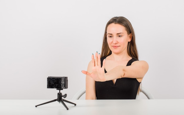 Młoda dziewczyna pozuje przy małym aparacie, pokazując gest stop na białym tle