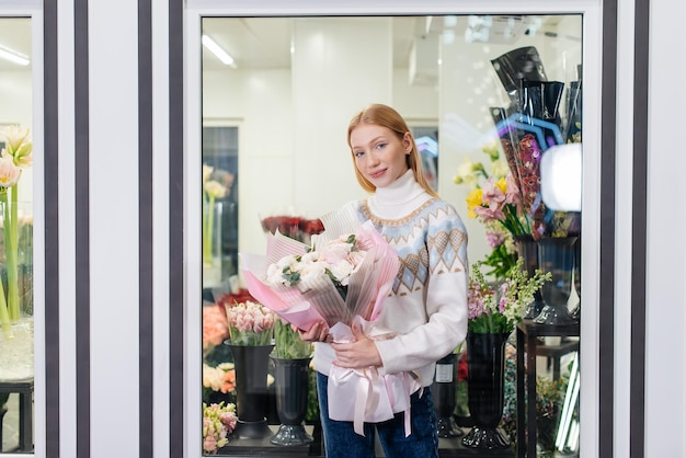 Młoda dziewczyna pozuje z pięknym świątecznym bukietem na tle przytulnej kwiaciarni Florystyka i tworzenie bukietów w kwiaciarni Mały biznes