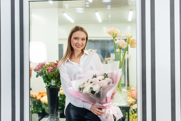 Młoda dziewczyna pozuje z pięknym świątecznym bukietem na tle przytulnej kwiaciarni Florystyka i tworzenie bukietów w kwiaciarni Mały biznes