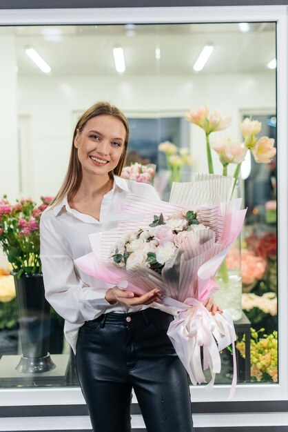 Młoda dziewczyna pozuje z pięknym świątecznym bukietem na tle przytulnej kwiaciarni Florystyka i tworzenie bukietów w kwiaciarni Mały biznes