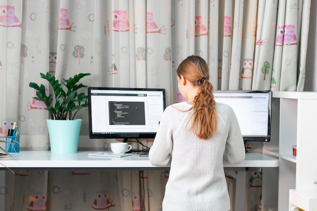 Młoda dziewczyna pracuje na komputerze przy stojącym biurku w domowym biurze Kształcenie na odległość e-learning praca w domu Wysoki stół biurkowy wygodny dla zdrowych pleców
