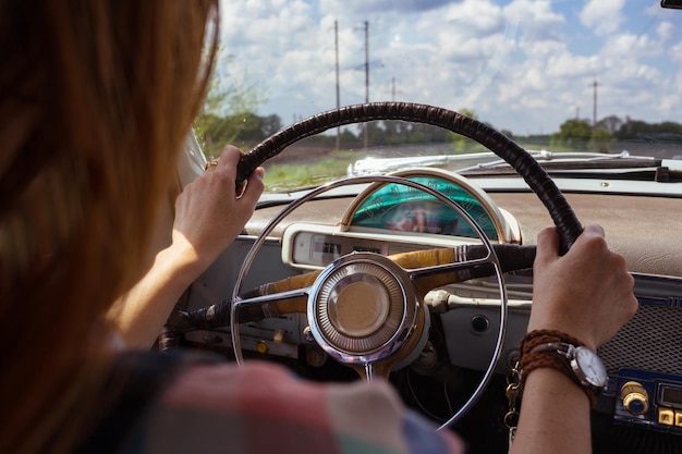 Młoda dziewczyna prowadząca retro samochód przy drodze na polach