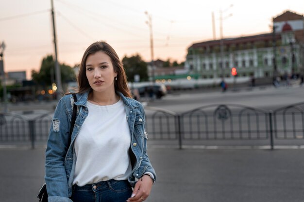 Młoda dziewczyna przy drodze. Portret studenta na tle miasta. Młoda stylowa kobieta, wieczorny spacer.