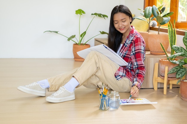 Młoda dziewczyna siedzi na podłodze i maluje na papierze w domu Hobby i studium sztuki w domu