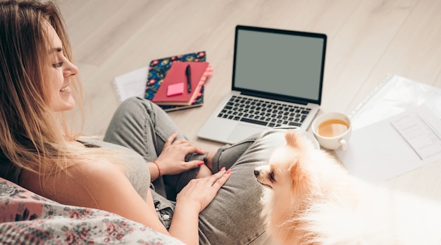 Młoda Dziewczyna Siedzi Na Podłodze Ze Swoim Psem Pomeranianem I Pracuje Na Laptopie. Pies Patrzy Na Nią