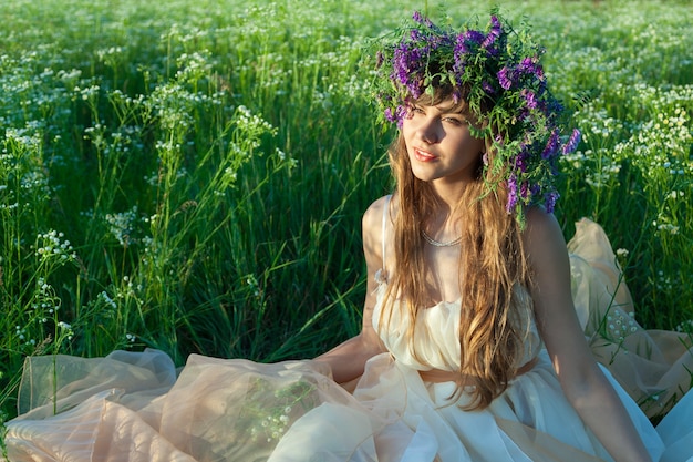 Młoda dziewczyna siedzi wśród kwiatów i trawy na polu.