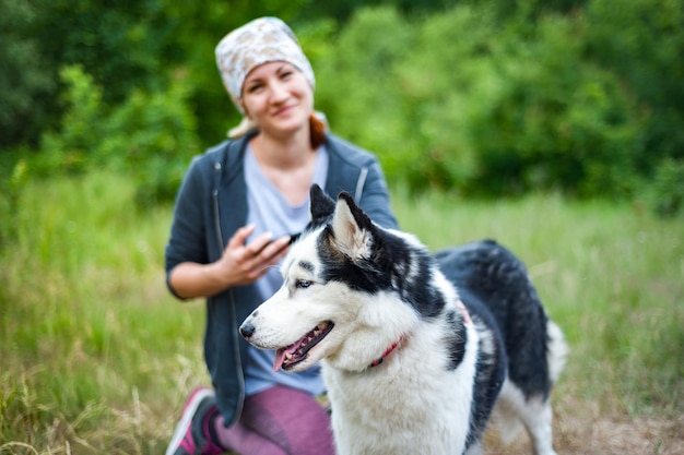 Młoda dziewczyna spacerując po parku z psem przytula psa Husky i całuje