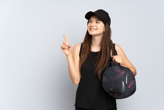 Młoda dziewczyna sportu z torbą sportową na szarym tle, wskazując na świetny pomysł