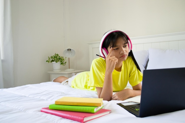 Młoda dziewczyna studiuje z laptopem na łóżku w sypialni