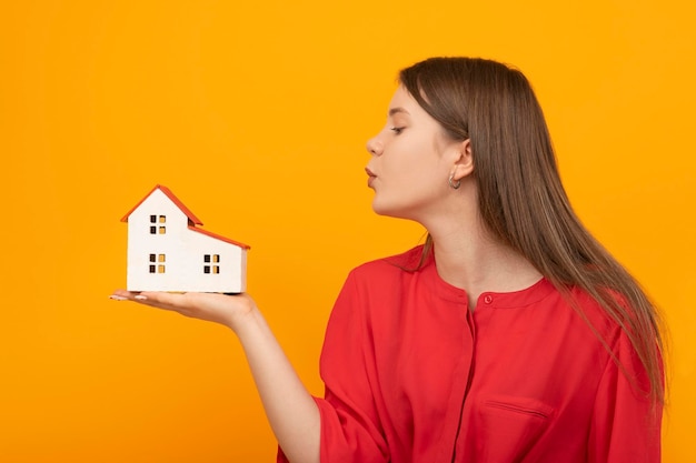 Zdjęcie młoda dziewczyna trzyma model domu w dłoni i wieje na niego portret kobiety z domkiem z zabawkami na żółtym tle nieruchomości lub nieruchomość