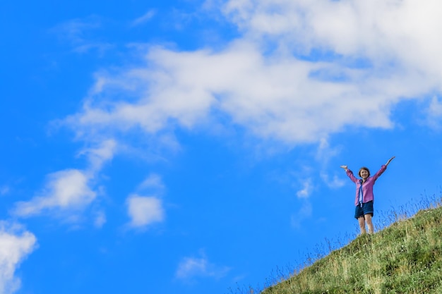 Młoda dziewczyna trzyma ręce na tle nieba i zbocza wzgórza