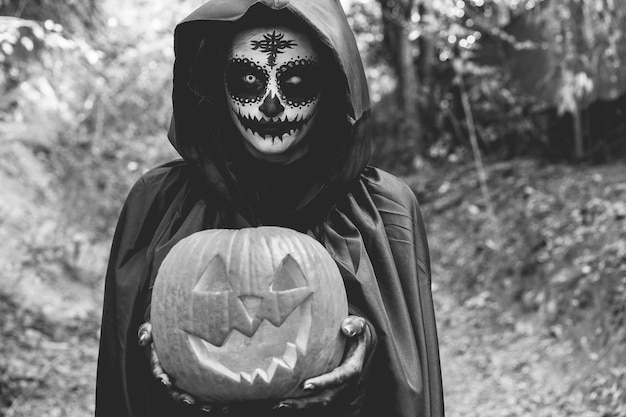 Zdjęcie młoda dziewczyna ubrana w tajemniczą sukienkę na halloween trzymającą straszną dynię skup się na twarzy edycja czarno-biała