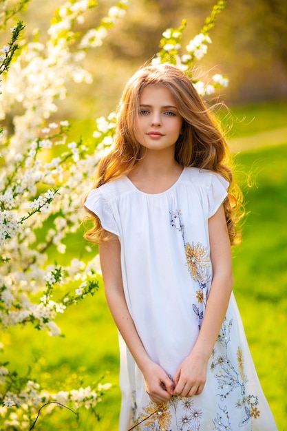 Zdjęcie młoda dziewczyna w białej sukni stoi w ogrodzie z kwiatami.
