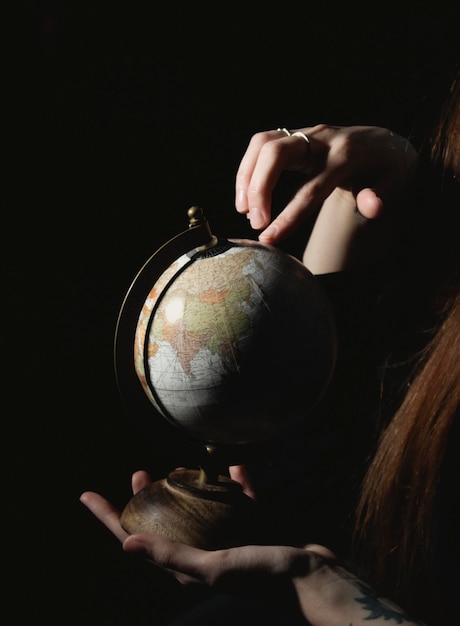 młoda dziewczyna w ciemnym pokoju trzymająca kulę ziemską w dłoniach i szukająca na niej krajów