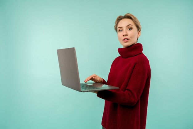 Młoda dziewczyna w czerwonym swetrze drukuje coś na laptopie na niebieskim tle