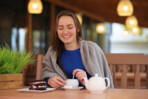 Młoda dziewczyna w kawiarni siedzi i pije herbatę z deserem