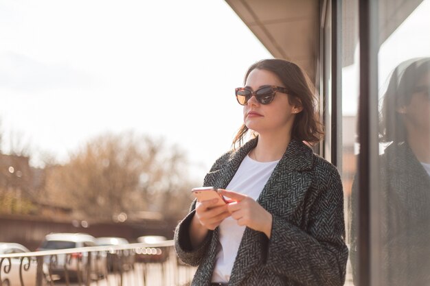 młoda dziewczyna w okularach przeciwsłonecznych trzyma smartphone na ulicy