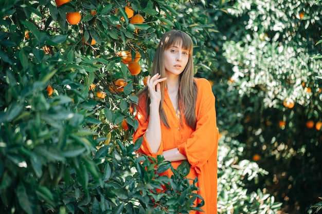Młoda dziewczyna w pomarańczowej sukience pozuje do kamery, trzymając lewą rękę w pomarańczowym ogrodzie