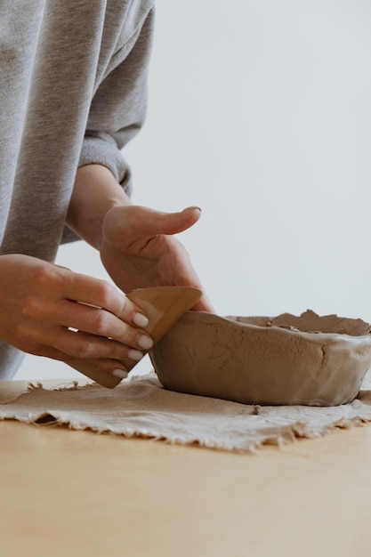 Młoda dziewczyna w szarym długim rękawie własnoręcznie robi wazon z gliny w pracowni rzeźbiarskiej