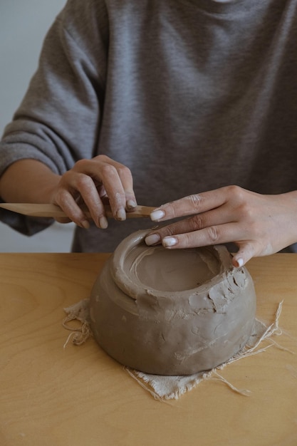 Młoda dziewczyna w szarym długim rękawie własnoręcznie robi wazon z gliny w pracowni rzeźbiarskiej
