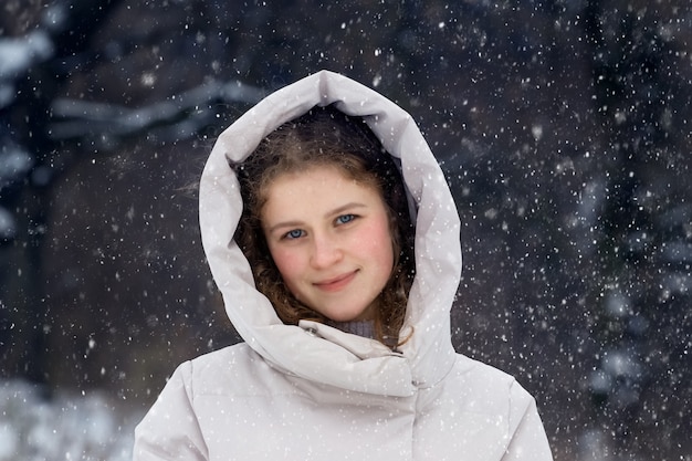 Młoda dziewczyna w zimowym lesie podczas opadów śniegu. Portret młodej szczęśliwej dziewczyny w zimowym lesie