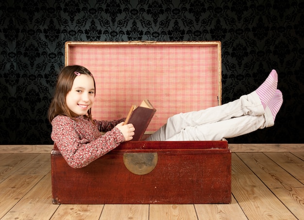 Młoda dziewczyna wśrodku antycznego bagażnika czyta książkę z rocznika tłem