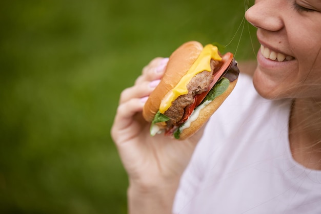 Młoda dziewczyna wyjmuje burgera z papierowej torby siedzącej na zielonej trawie