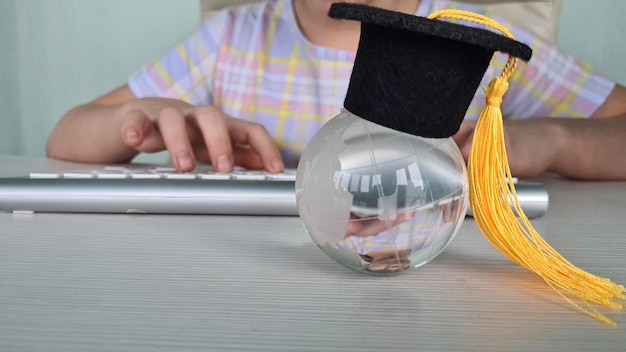 Zdjęcie młoda dziewczyna z czapką do ukończenia studiów pisze na laptopie ze szklanym globusem koncepcja elearning