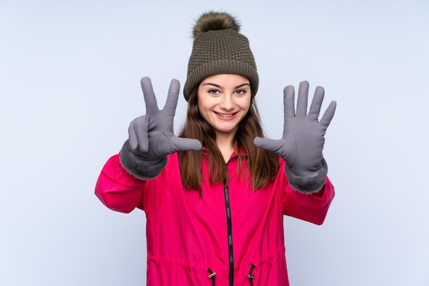 Młoda dziewczyna z czapka zimowa na niebieską ścianą licząc osiem palcami