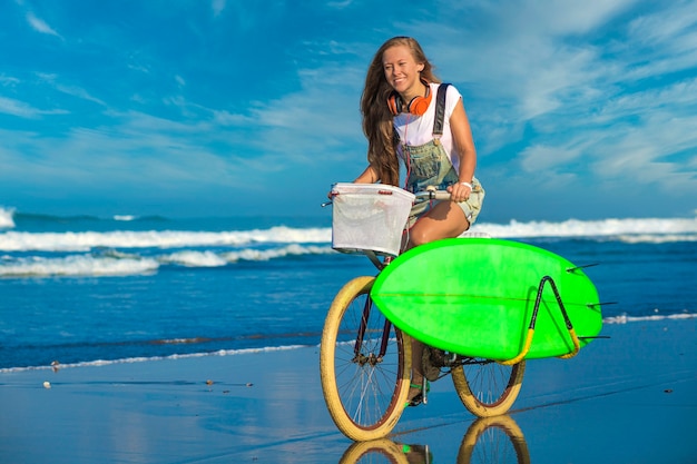 Młoda dziewczyna z deską surfingową i rowerem na plaży