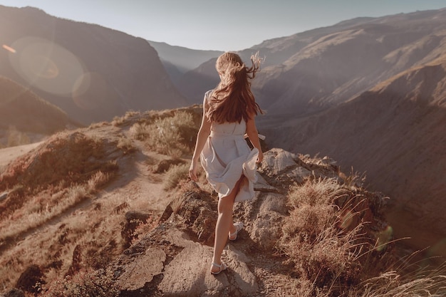Zdjęcie młoda dziewczyna z długimi włosami ubrana w stylową sukienkę wspina się na wzgórze, aby popatrzeć na piękny górski krajobraz