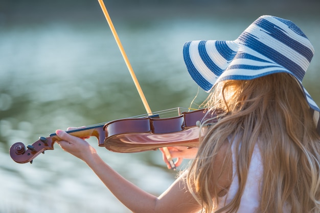 Młoda dziewczyna z kapeluszem bawić się skrzypce przy jeziorem.