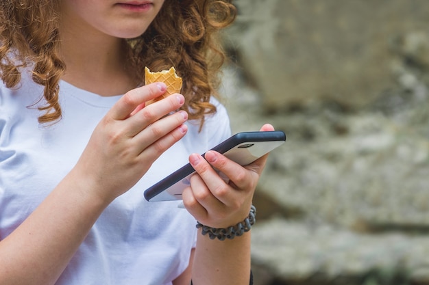 Zdjęcie młoda dziewczyna z kręconymi włosami trzyma telefon w ręku i zjada lody