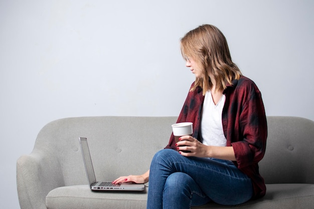 Młoda dziewczyna z laptopem siedzi na kanapie i pije kawę Kobieta używa komputera