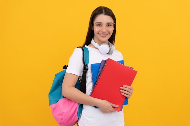 Młoda dziewczyna z plecakiem i słuchawkami trzyma skoroszyt na żółtym tle z powrotem do szkoły
