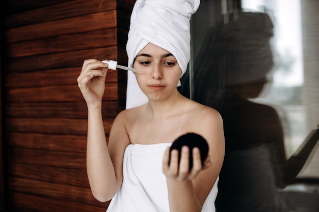 Młoda dziewczyna z ręcznikiem na głowie wykonuje zabiegi na twarz Pielęgnacja skóry nawilżająca serum