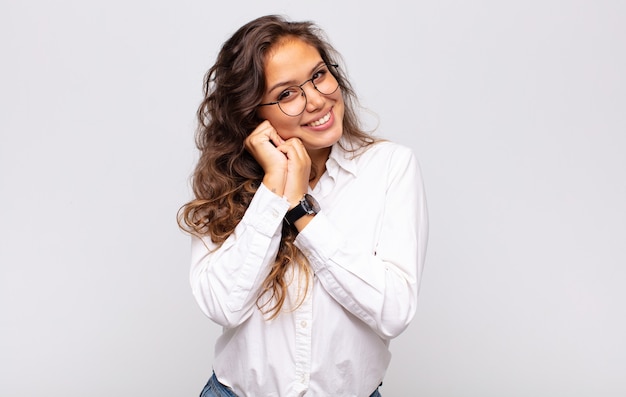 młoda ekspresyjna kobieta w okularach i elegancka biała bluzka pozuje na białej ścianie