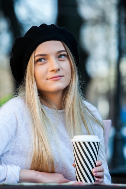 Zdjęcie młoda, elegancka kobieta pije herbatę na ulicy, hipsterka, europejska dziewczyna z szklanką papierową do latte.