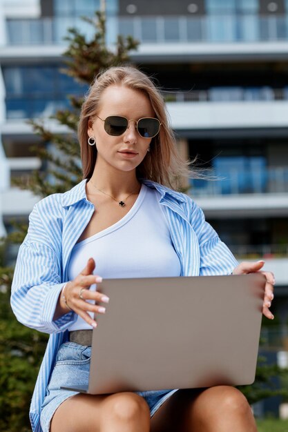 Młoda Europejka pracuje w branży informatycznej i korzysta z laptopa, siedząc na ulicy.