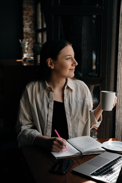 Młoda europejska freelancerka z długimi ciemnymi włosami pracuje zdalnie i studiuje w kawiarni