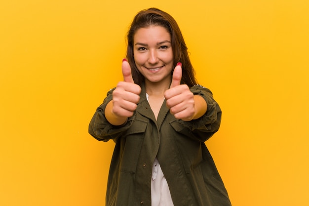 Zdjęcie młoda europejska kobieta nad żółtą ścianą z kciukami do góry, kibicuje o czymś