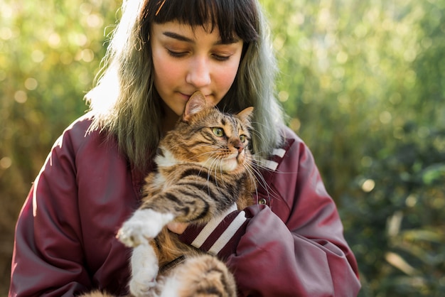 Młoda farbowana włosiana kobieta ściska jej tabby kota w parku