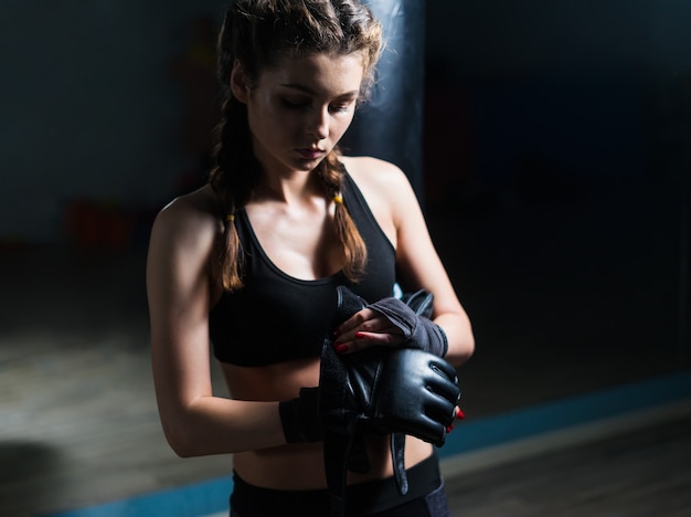 Młoda fighter bokser model dziewczyna zakładanie rękawic bokserskich przed treningiem.
