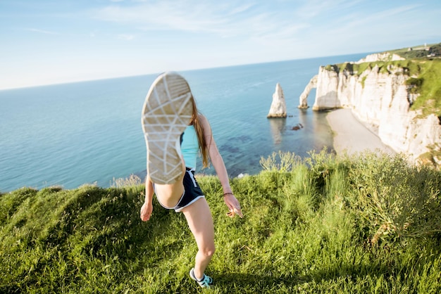 Młoda figlarna kobieta w stroju sportowym kopie z nogami na tle skalistego wybrzeża