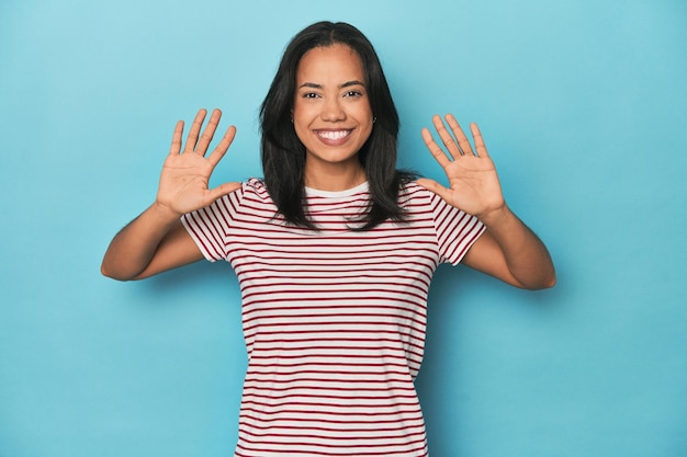 Młoda filipińska kobieta w niebieskim studiu pokazująca numer dziesięć z rękami