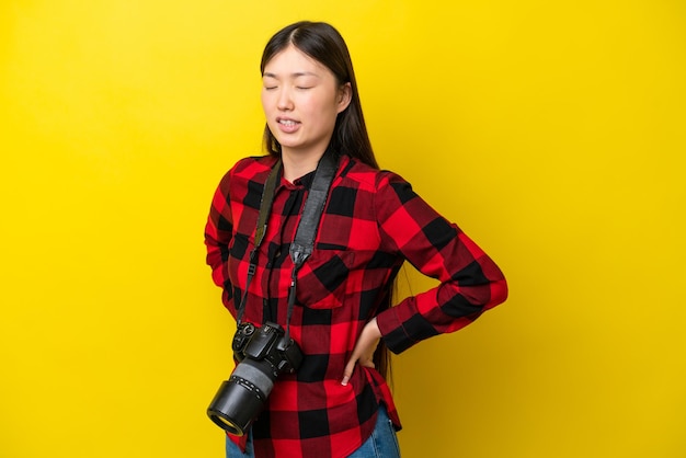 Młoda fotografka Chinka odizolowana na żółtym tle cierpi na ból pleców za wysiłek