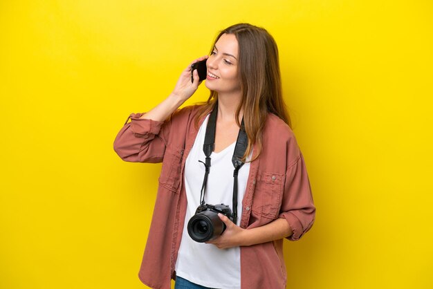 Młoda fotografka kaukaska kobieta odizolowana na żółtym tle, prowadząca rozmowę z telefonem komórkowym