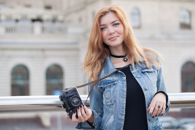 Młoda fotografka spacerująca ulicą w dżinsowej kurtce ze starym aparatem