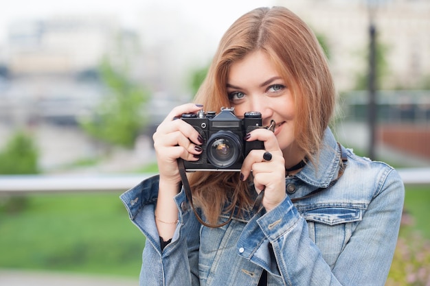Młoda fotografka spacerująca ulicą w dżinsowej kurtce ze starym aparatem