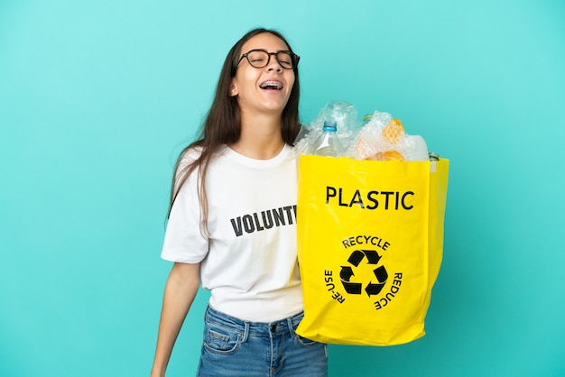 Młoda francuska dziewczyna trzyma torbę pełną plastikowych butelek do recyklingu, śmiejąc się